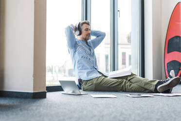 Businessman wearing wireless headphones and relaxing in office - UUF30935