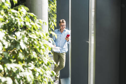 Lächelnder Geschäftsmann, der ein Smartphone im Büro benutzt - UUF30937