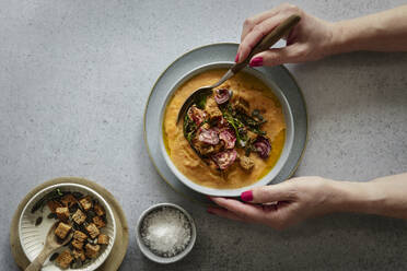 Hands of woman eating bowl of pumpkin soup - EVGF04449