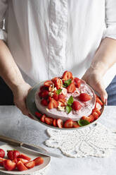 Hände einer Frau halten einen Teller mit verzehrfertiger veganer Erdbeertorte - EVGF04457