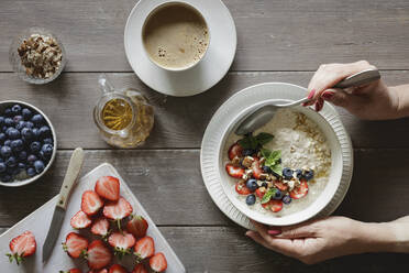 Hands of woman eating bowl of porridge with blueberries and strawberries - EVGF04460