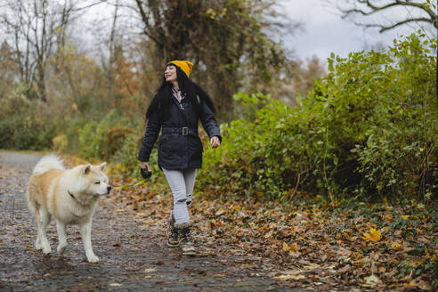 Lächelnde Frau mit Hund auf dem Fußweg im Herbstpark - JCCMF11069