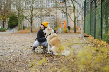 Happy woman petting Akita dog at autumn park - JCCMF11071