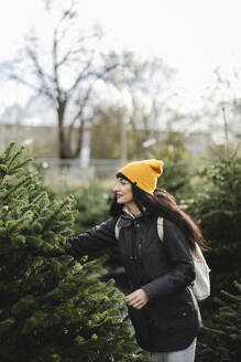 Woman wearing knit hat and buying fir tree - JCCMF11077