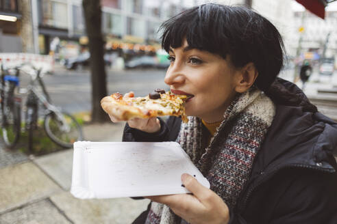 Happy woman eating slice of pizza at sidewalk cafe - JCCMF11085