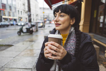 Smiling beautiful woman holding disposable coffee cup at street - JCCMF11088