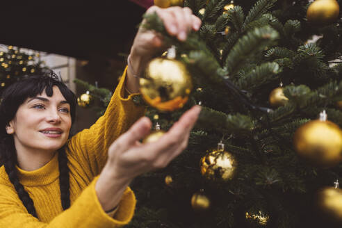 Glückliche Frau beim Schmücken des Weihnachtsbaums mit Ornamenten - JCCMF11098