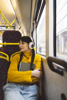 Frau mit drahtlosen Kopfhörern und Tablet-PC auf dem Sitz im Bus sitzend - JCCMF11102