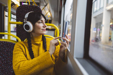 Smiling woman wearing wireless headphones and photographing through smart phone - JCCMF11104