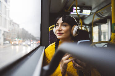 Thoughtful woman sitting with smart phone in bus - JCCMF11105