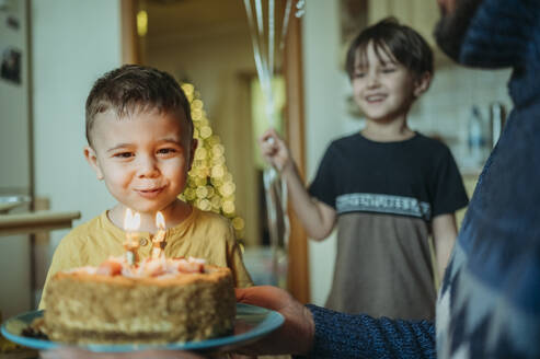 Geburtstagskind bläst Kerzen auf Kuchen zu Hause aus - ANAF02629