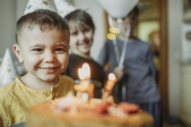 Glücklicher Junge mit Geburtstagstorte und Geschwistern im Hintergrund - ANAF02632