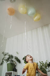 Excited boy playing with balloons at home - ANAF02635