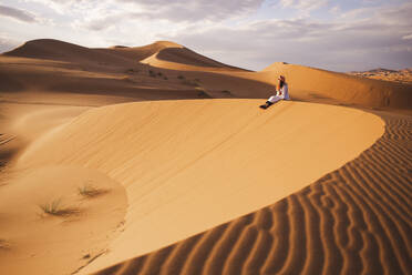 Young woman sitting on sand dune at Sahara desert in Morocco, Africa - PCLF00912