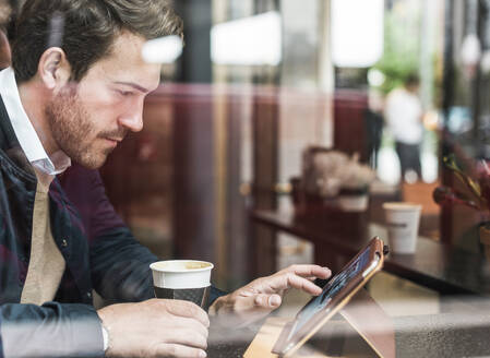 Young businessman with coffee cup using tablet PC at cafe - UUF30941