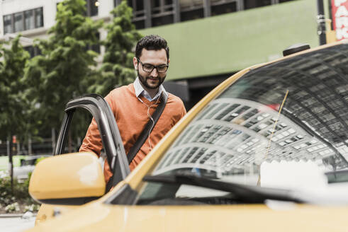 Businessman wearing eyeglasses and getting into taxi - UUF30949