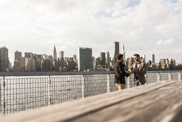 Young business colleagues talking by Hudson river at sunset in New York City, USA - UUF30960