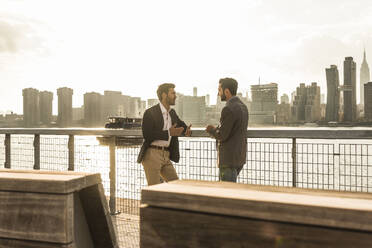 Geschäftskollegen lehnen an einem Geländer und unterhalten sich in der Nähe der Skyline von New York City, USA - UUF30961
