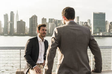 Lächelnder Geschäftsmann im Gespräch mit einem Kollegen am Hudson River in New York City, USA - UUF30963