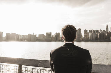 Businessman looking at city view by Hudson River, New York City, USA - UUF30965