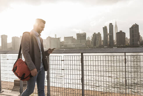 Geschäftsmann mit Smartphone und Spaziergang am Fluss in New York City, USA - UUF30972