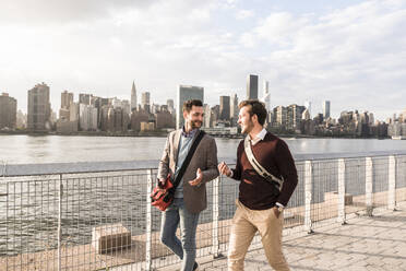 Happy young colleagues talking by river in front of skyline of New York City - UUF30973