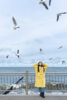 Unbeschwerte Frau, die sich in der Nähe des Meeres amüsiert, mit Möwen, die durch die Luft fliegen - OLRF00086
