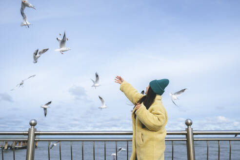 Woman reaching at seagulls flying near sea - OLRF00087