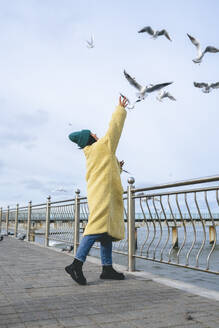 Frau steht am Geländer und greift nach Möwen, die in der Nähe des Meeres fliegen - OLRF00088