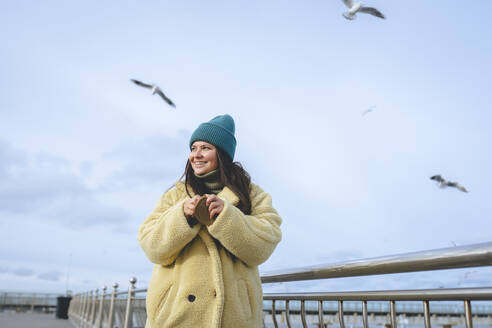 Smiling woman wearing warm clothes and standing near railing - OLRF00090