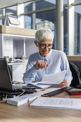 Geschäftsfrau prüft Dokument am Arbeitsplatz - IKF01524