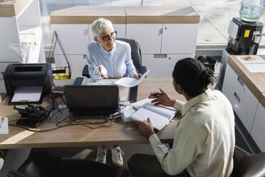 Geschäftsfrau bespricht sich mit einem Kollegen am Schreibtisch im Büro - IKF01532