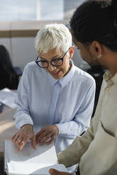 Businesswoman planning strategy with colleague holding diary at office - IKF01548