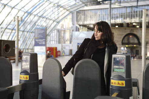 Mature woman scanning ticket at railway station - ASGF04811