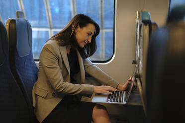 Mature businesswoman working on laptop in train - ASGF04822
