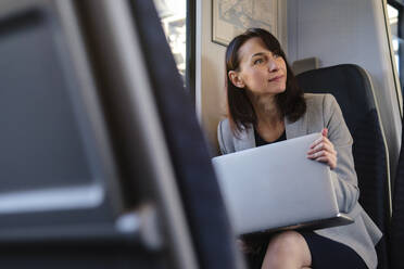 Businesswoman sitting with laptop in train - ASGF04824