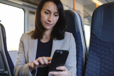 Businesswoman using smart phone in train - ASGF04825