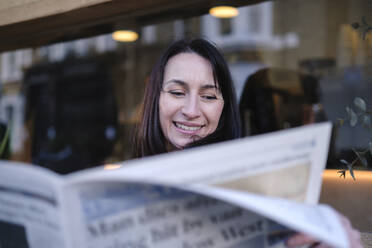 Glückliche Frau, die vor einem Gebäude Zeitung liest - ASGF04849