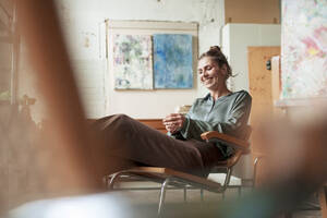 Happy painter sitting on chair in art studio - JOSEF22773