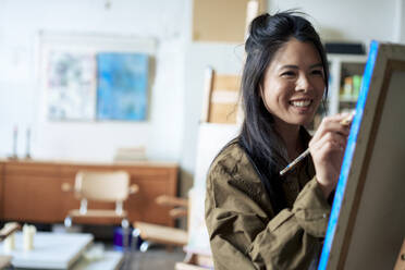 Smiling painter painting on canvas in art studio - JOSEF22819