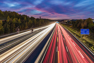 Deutschland, Baden-Württemberg, Leonberg, Fahrzeuglichtspuren entlang der Bundesautobahn 8 in der Abenddämmerung - WDF07503