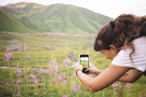 Junge Frau fotografiert blühende Pflanzen mit ihrem Smartphone - PCLF00938