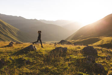 Frau springt auf Felsen vor Bergen bei Sonnenuntergang - PCLF00943