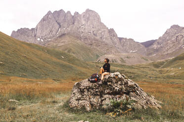 Frau sitzt mit Rucksack auf einem Felsen vor dem Berg Kazbek - PCLF00953