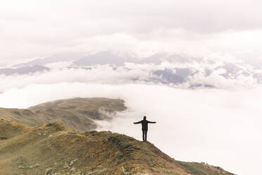 Woman with arms outstretched standing on Mestia mountain near clouds - PCLF00964