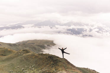 Carefree woman standing on Mestia mountain cliff near clouds - PCLF00965