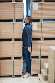 Businessman hiding between stacks of panels at factory workshop - JOSEF22888