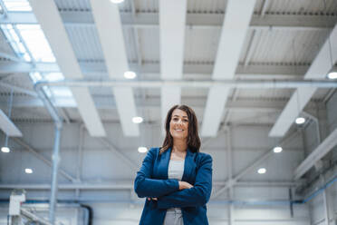 Smiling businesswoman with arms crossed standing in workshop - JOSEF22905