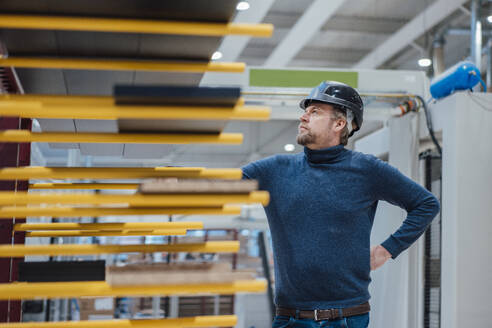 Thoughtful businessman wearing hardhat standing in industry - JOSEF22966