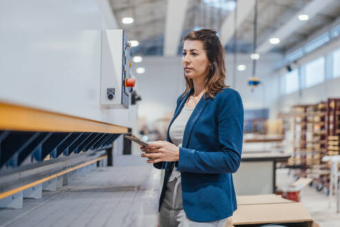 Geschäftsfrau mit Tablet-PC bei der Überprüfung von Maschinen in einer Werkstatt - JOSEF22971